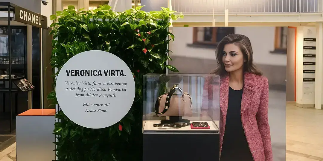 En utställning med Veronica Virta, en växtvägg, en skylt och en bild av en kvinna i en rosa kavaj.